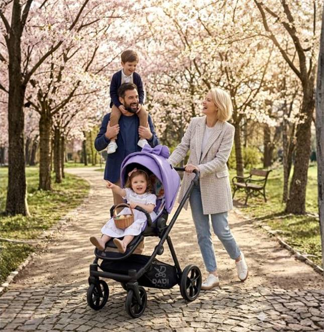 Rodzina spacerująca z wózkiem Natoni Joy New w kolorze fioletowym Veri Peri w parku z kwitnącymi drzewami